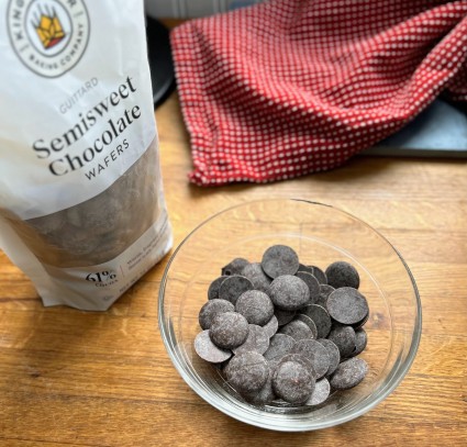A bag of chocolate wafers, with some poured into a small glass bowl.