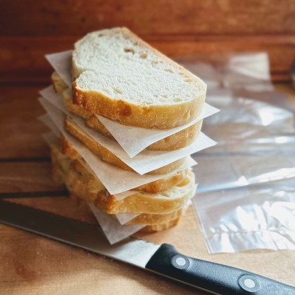 Individual slices of sourdough bread separated by pieces of parchment piled on a cutting board.
