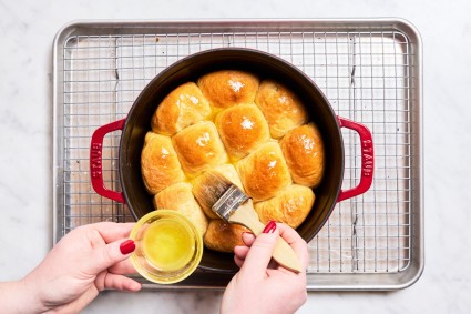 Brush melted butter over baked dinner rolls in Dutch oven