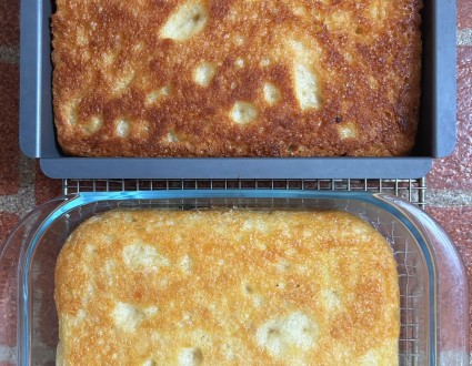 Two focaccias, one in a black metal pan, one in a clear glass pan, turned upside down to show their bottom crusts.