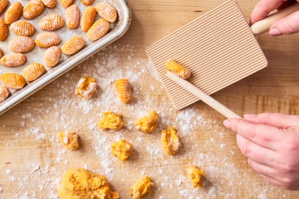 Hands shaping sweet potato gnocchi dough with a gnocchi board