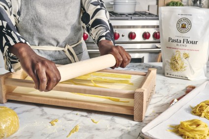 Pasta being pushed through a chitarra pasta cutter