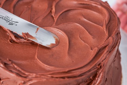 Smooth chocolate frosting being applied to cake with an offset spatula
