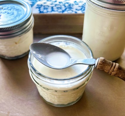 Heavy cream and yogurt stirred together in a small glass jar, prior to fermentaiton, showing the mixture's liquid texture.