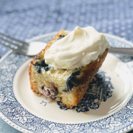 Blueberry muffin cake on a plate with a dollop of creme fraiche on top. 