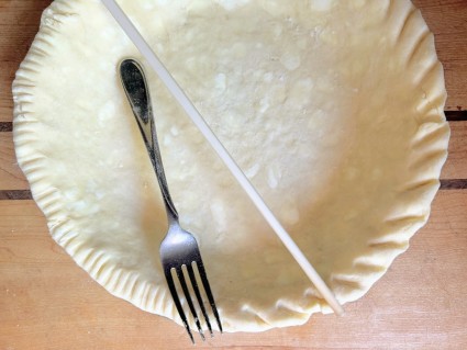 Pastry dough in a 9" pie pan showing two types of crimp around the edge: one made with a fork, one with a chopstick.