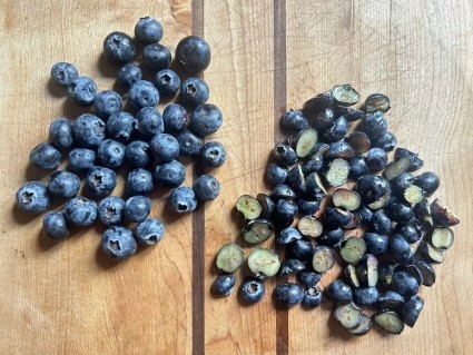 Two piles of blueberries on a wooden board, one pile whole berries, one chopped berries.