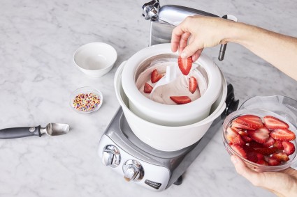 Overhead shot of strawberries being added to the ice cream maker attachment.