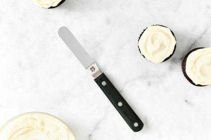 Small offset spatula next to a frosted cupcake and a bowl of frosting