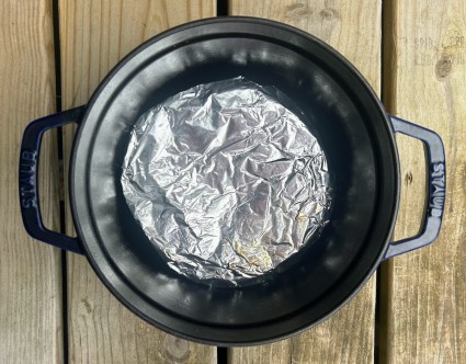 A Dutch oven with a black interior showing a bottom liner of crumpled, flattened aluminum foil.