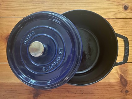 A Dutch oven sitting on a wooden counter, showing its black enameled interior.