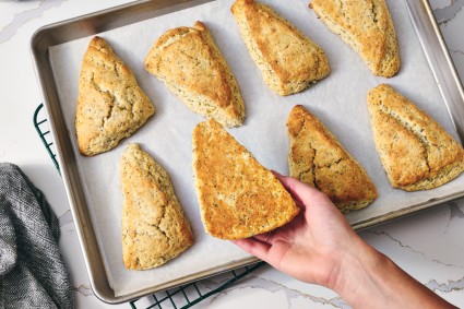 Hand showing well-browned bottom of a lemon poppy seed scone baked on nested sheet pans