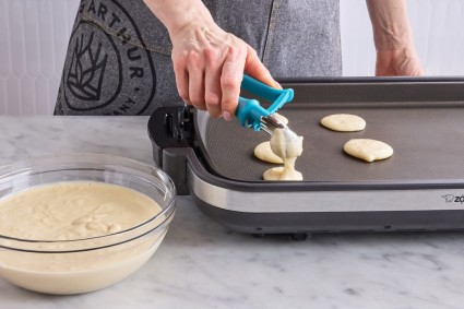 Scooping pancake batter onto griddle with teaspoon scoop