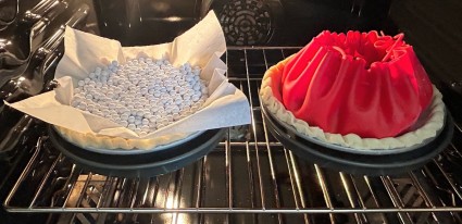 Two pie crusts, one lined with a silicone pie pouch, one with parchment and rice, baking in an oven.