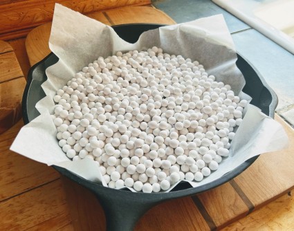 Ceramic weights in a parchment sling, sitting in a cast iron frying pan to cool.