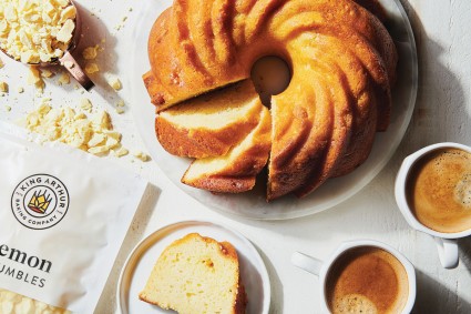 A Lemon Buttermilk Bundt Cake with a few slices removed and on small plates next to an open bag of Lemon Crumbles