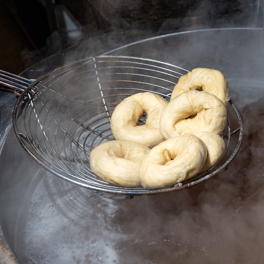 A wire ladle pulling bagels from a pot of boiling water. - select to zoom