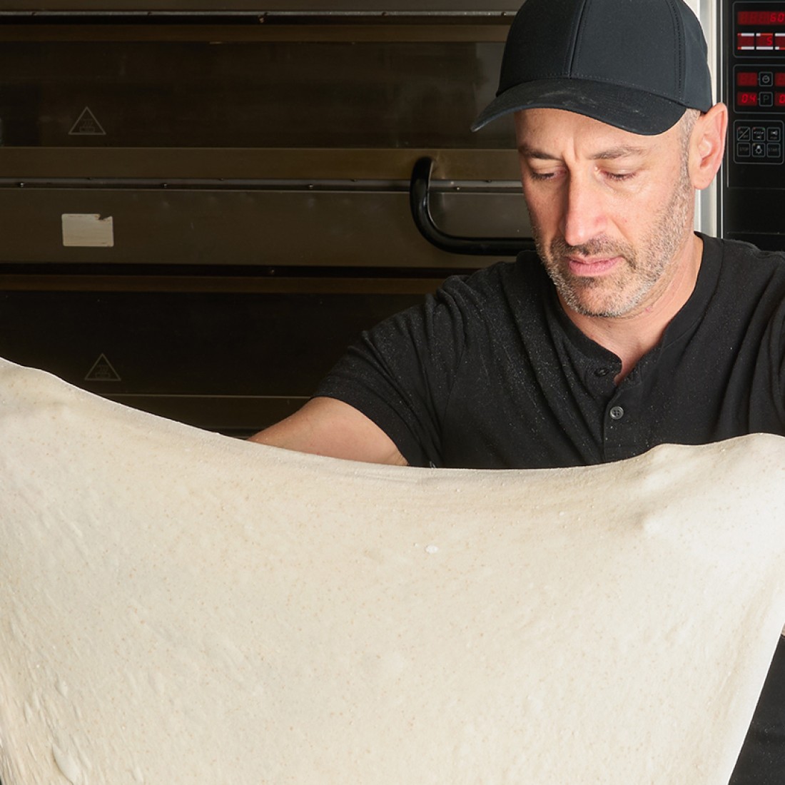 A person stretching a large pizza dough in their hands. - select to zoom