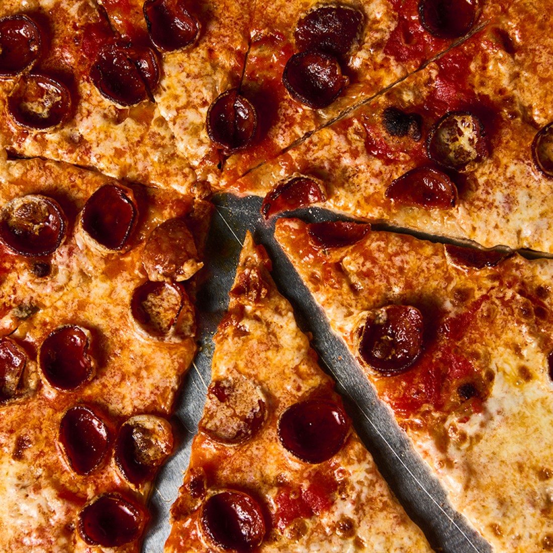 Close up photograph of a pepperoni pizza sliced and seen from above. - select to zoom