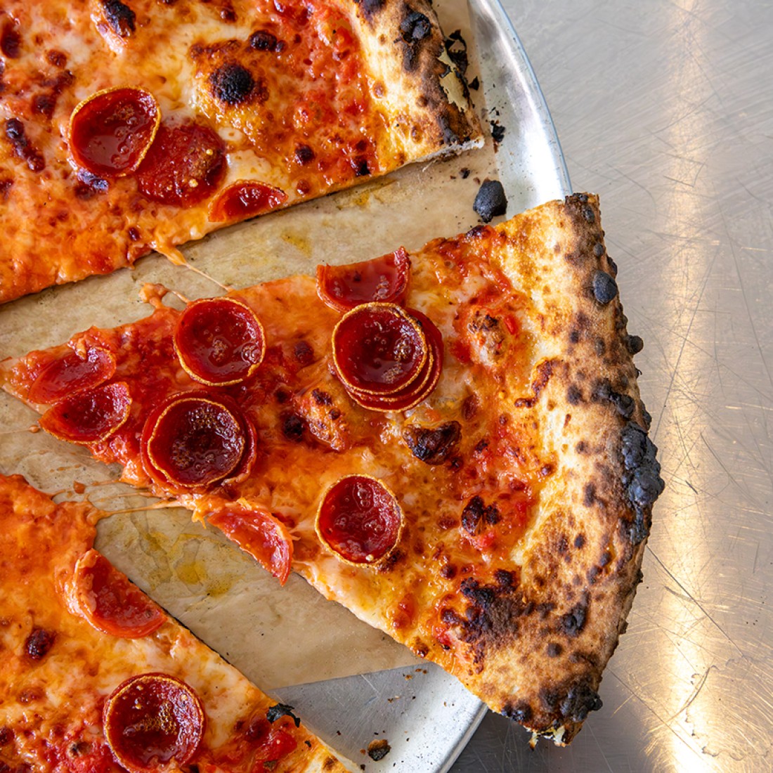 A slice of pepperoni pizza slightly offset from the rest of the pizza photographed from above. - select to zoom