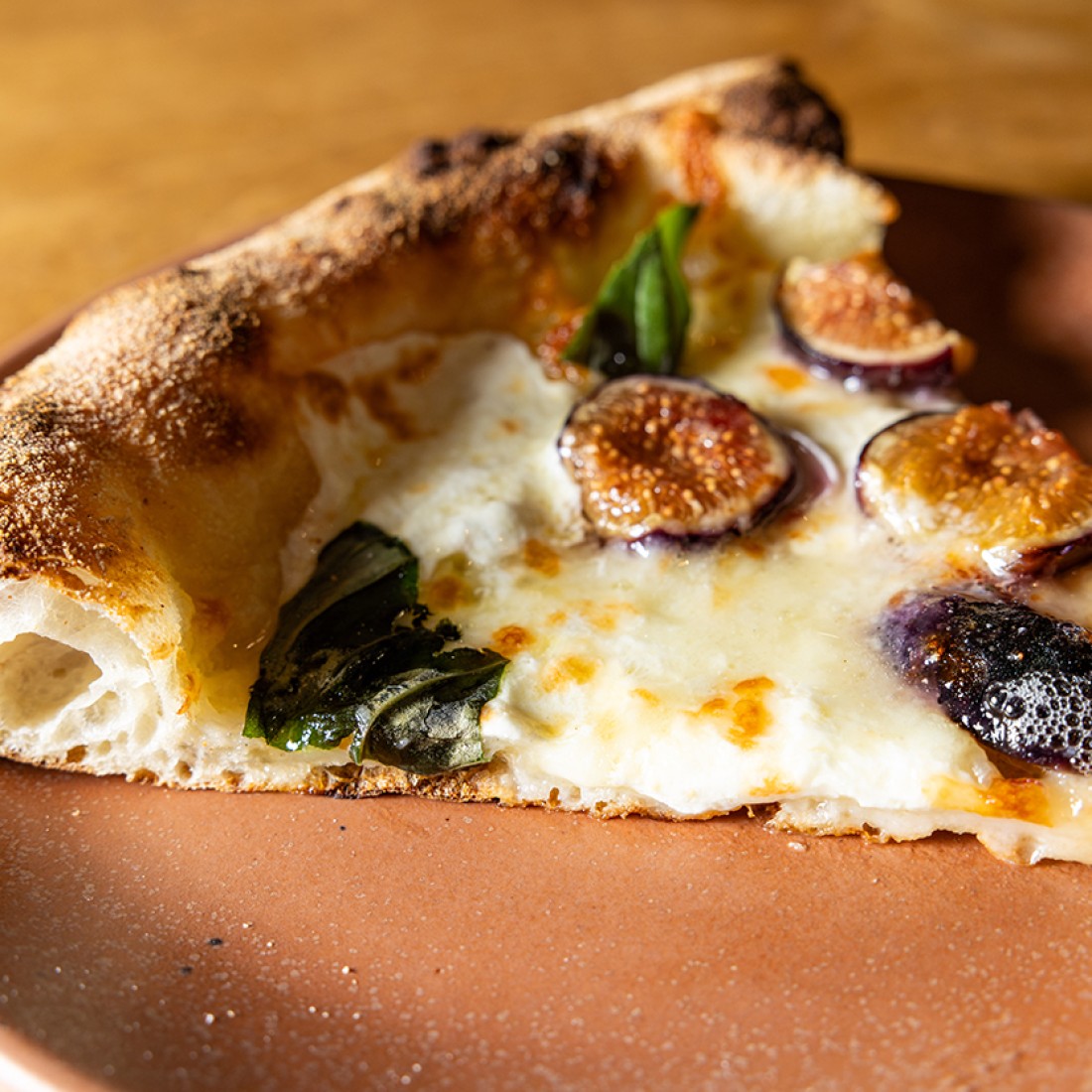 A slice of cheesy pizza with dates and basil baked into the melted cheese. - select to zoom