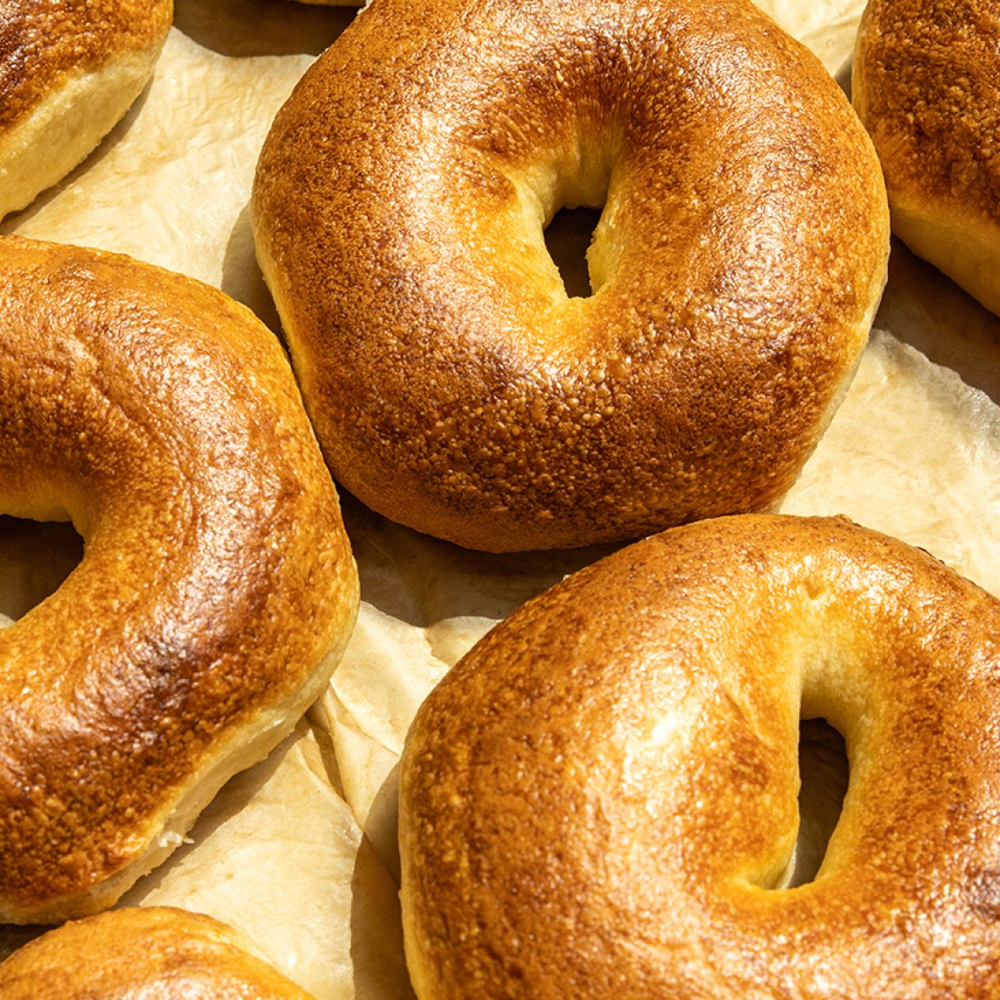 Photograph of golden cooked bagels spread on a baking sheet. - select to zoom