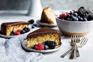 Two slices of yellow cake topped with fudge frosting on plates, garnished with fresh berries