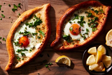 Two freshly baked Khachapuri (Georgian Cheese Breads) topped with soft-baked eggs and fresh herbs