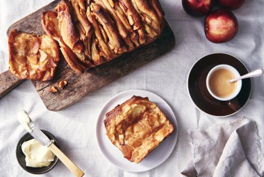 A loaf of Cinnamon Apple Pull-Apart Bread with one slice pulled off, on a plate next to a cup of coffee