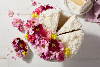 A Old-Fashioned Coconut Cake coated in shredded coconut and decorated with a spray of edible flowers