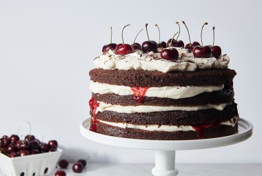 A Black Forest Cake made from layers of chocolate cake and topped with fresh cherries, on a cake stand