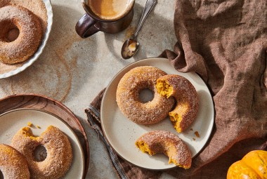 A few baked pumpkin donuts dusted in cinnamon sugar on plates, ready to be eaten.