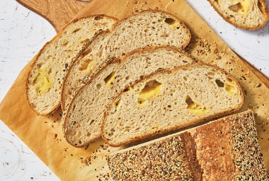 Parmesan Black Pepper Sourdough Bread sliced and laid out on a wooden cutting board showing an airy bread with cheese in the air pockets.