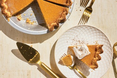 A slice of Smooth and Spicy Pumpkin Pie on a plate with the full pie in the background