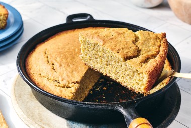 A slice of Sourdough Cornbread being removed from a cast iron skillet.