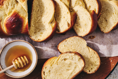 Challah bread sliced and shown on a counter with a bowl of honey next to the slices.
