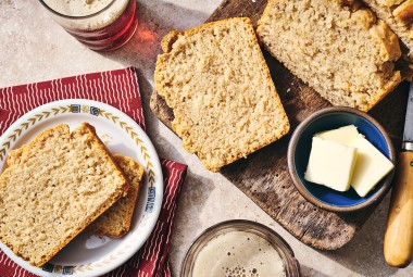 Sliced classic beer bread on a table with butter and a cutting board.